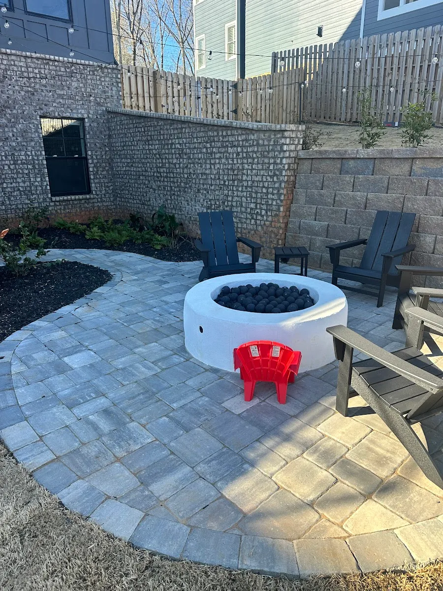 Curved paver patio with a modern fire pit and hardscape backdrop