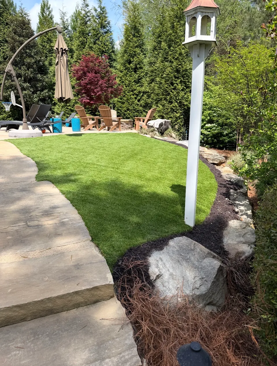 Finished backyard with turf, stone path, patio seating, and landscape beds