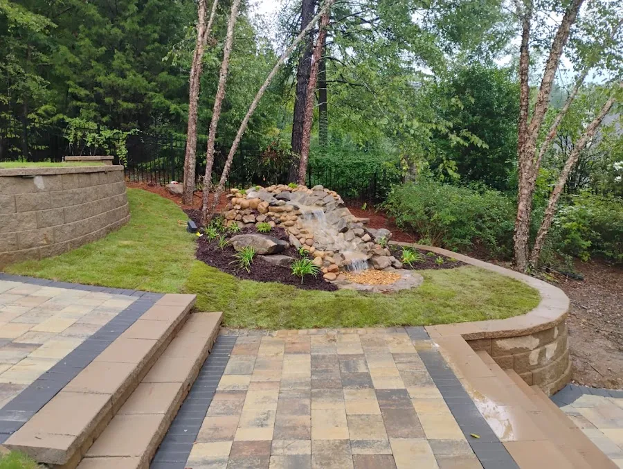 Hardscape patio edge with stone wall, planting beds, and a small water feature